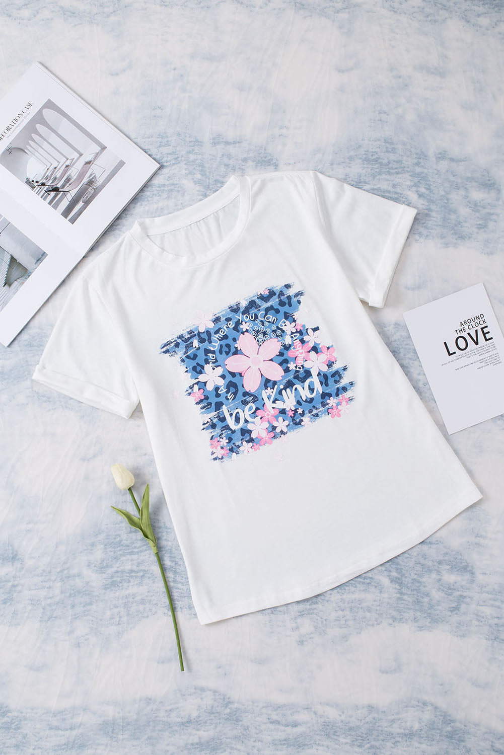 White graphic tee with floral accents and "be kind" text, casual short sleeve.