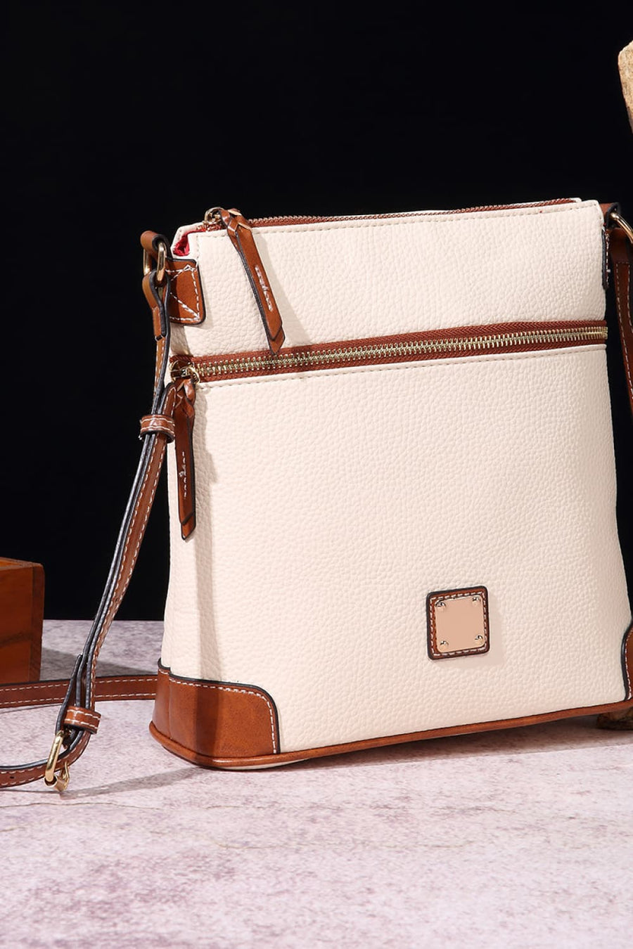 Ivory leather crossbody bag with brown trim and gold hardware, featuring two zip compartments.
