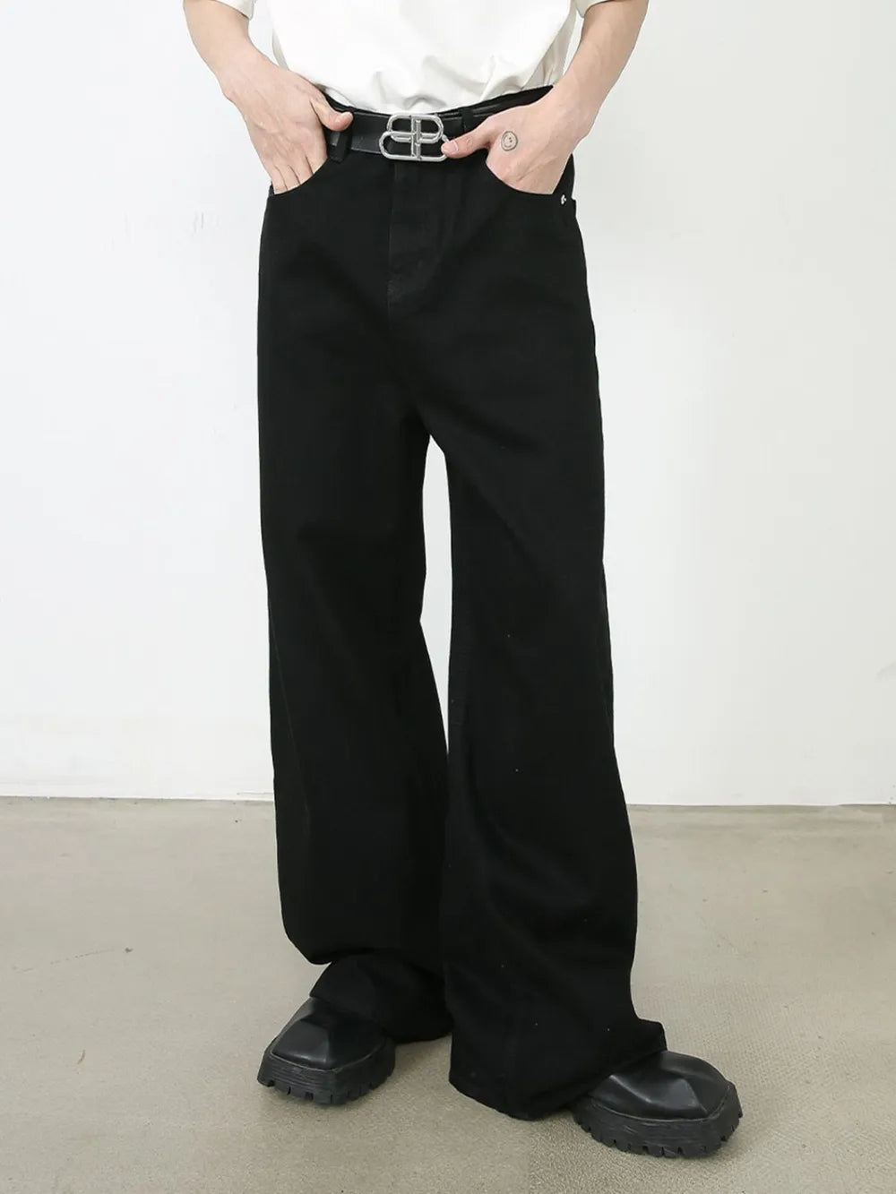 Black denim palazzo trousers with a wide leg and buttoned waist, styled with a belt.
