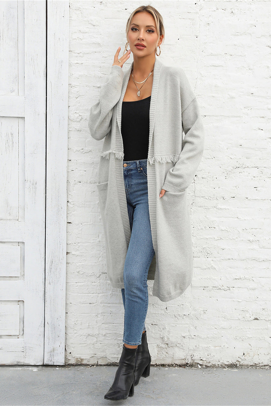 Light gray longline knit cardigan with fringe trim and pockets, open front, long sleeves.