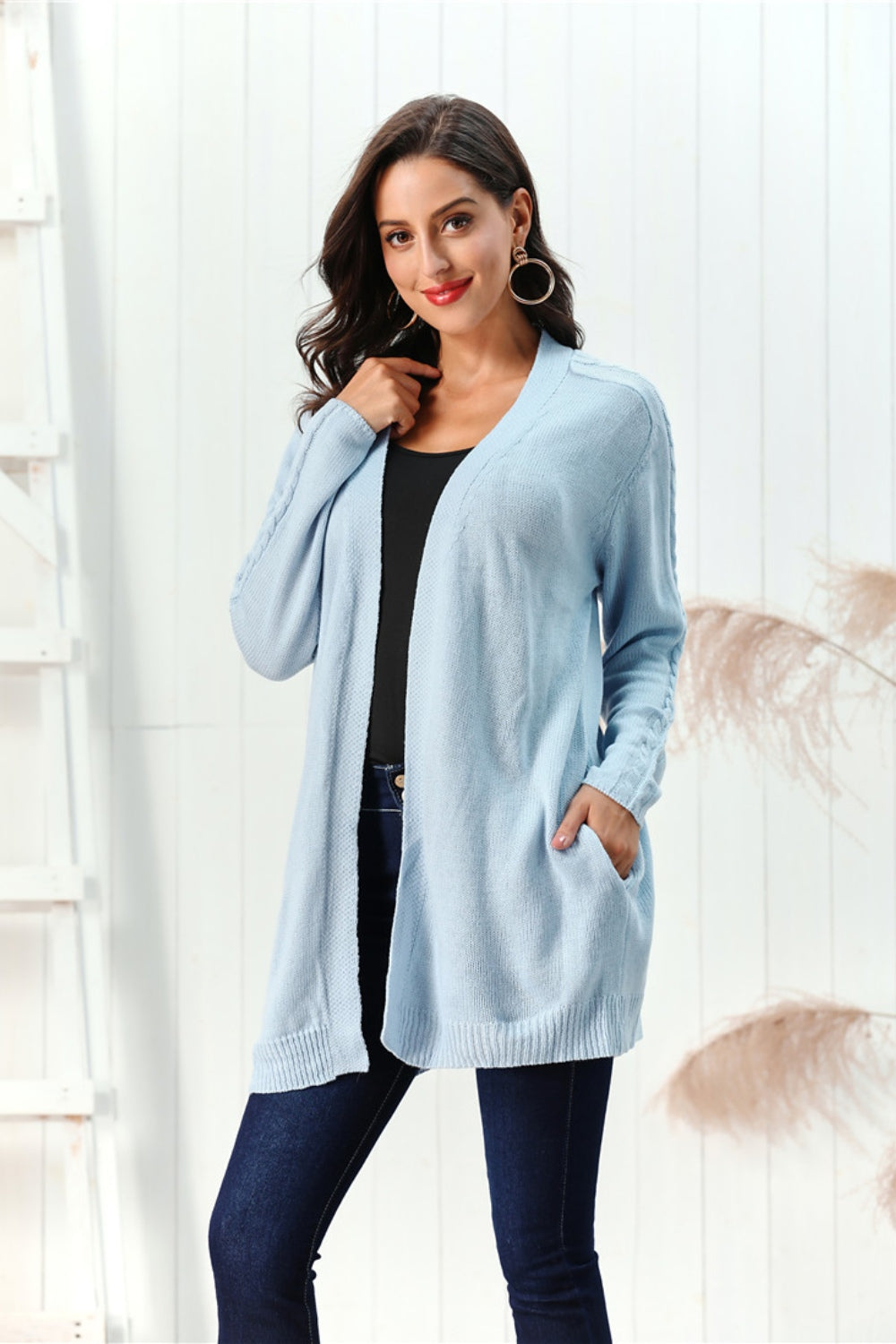 Light blue cable knit open front cardigan with pockets and braided sleeve detail.