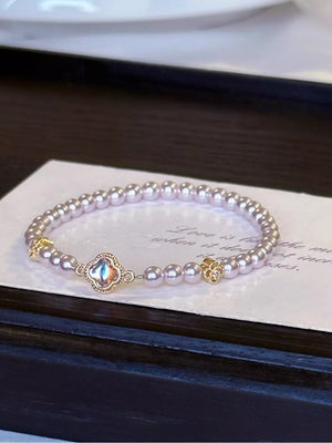 Delicate pearl bracelet with gold clover charm and iridescent center stone.