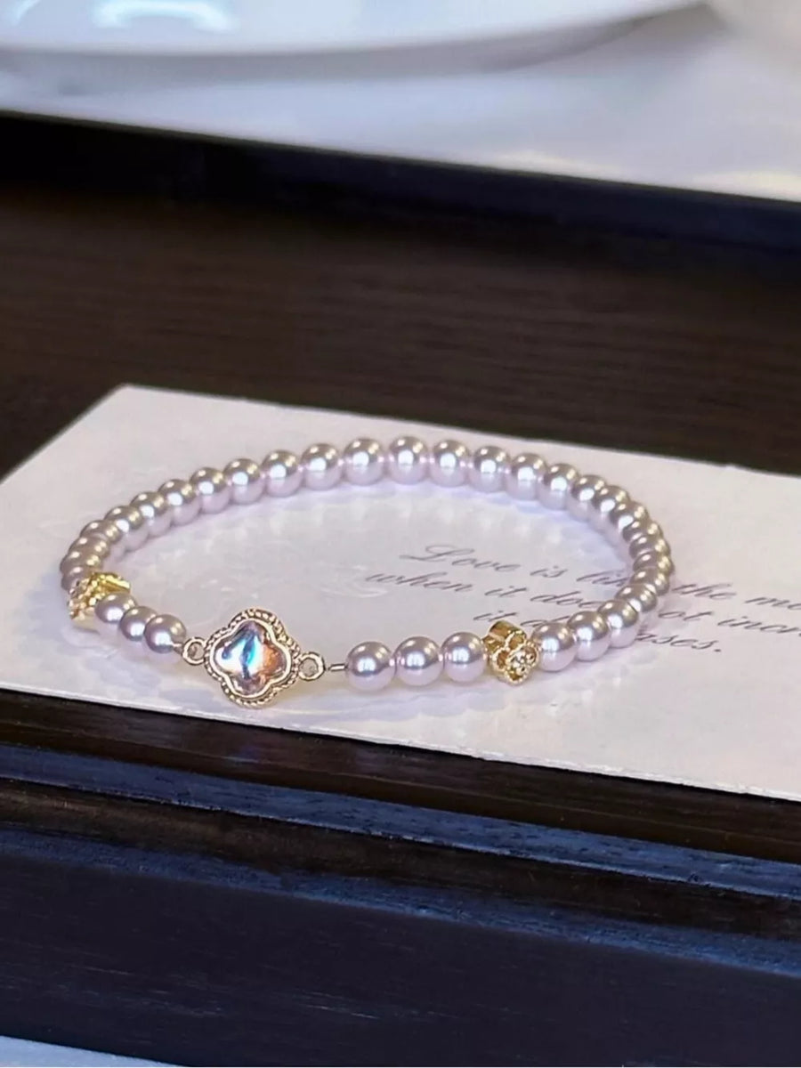 Delicate pearl bracelet with gold clover charm and iridescent center stone.
