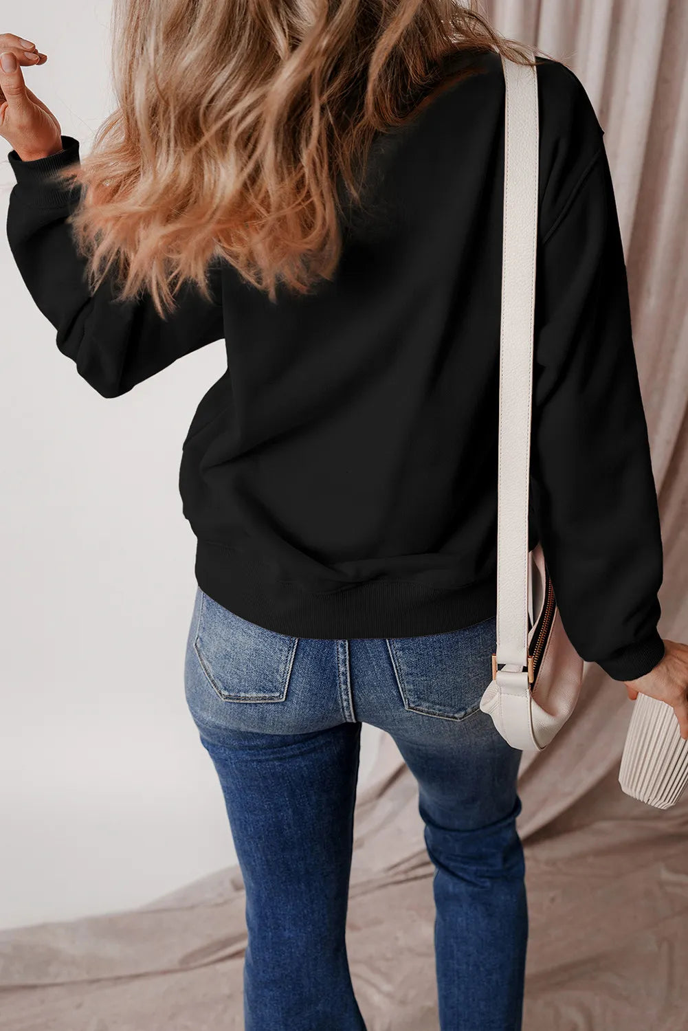 Black crewneck sweatshirt with long sleeves and ribbed cuffs, styled with jeans.