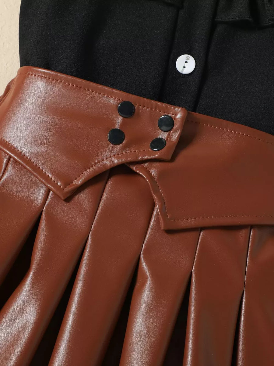 Black baby top with white button detail and brown faux leather pleated skirt with snap closures.
