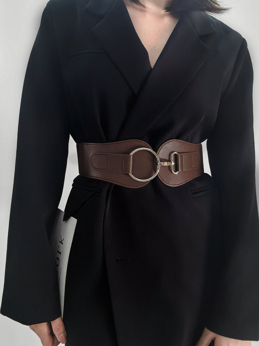 Brown elastic waist belt with sculpted buckle detail and silver hardware cinching a black blazer.