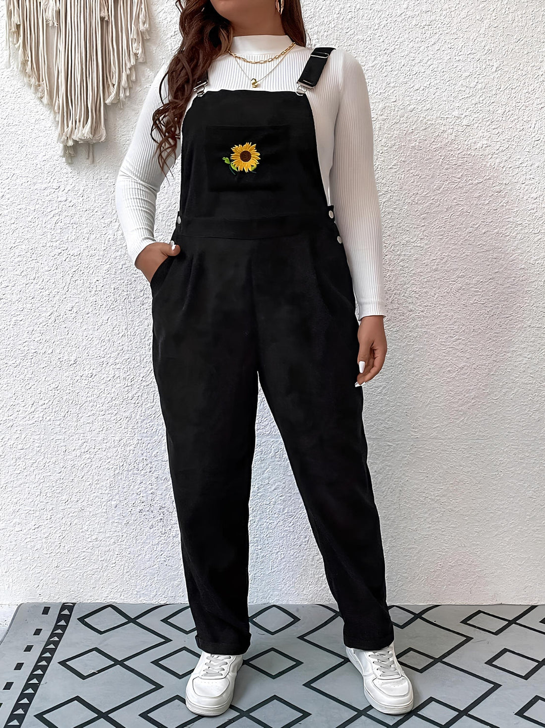 Black corduroy overalls with embroidered sunflower detail and relaxed fit.