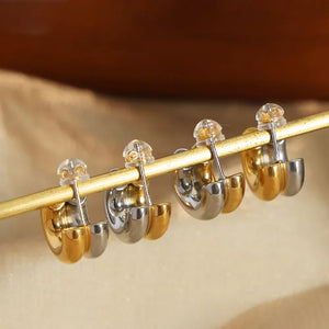 Dual-tone sculptural C-hoop earrings in gold and silver with clear backs.