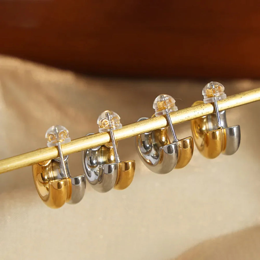 Dual-tone sculptural C-hoop earrings in gold and silver with clear backs.