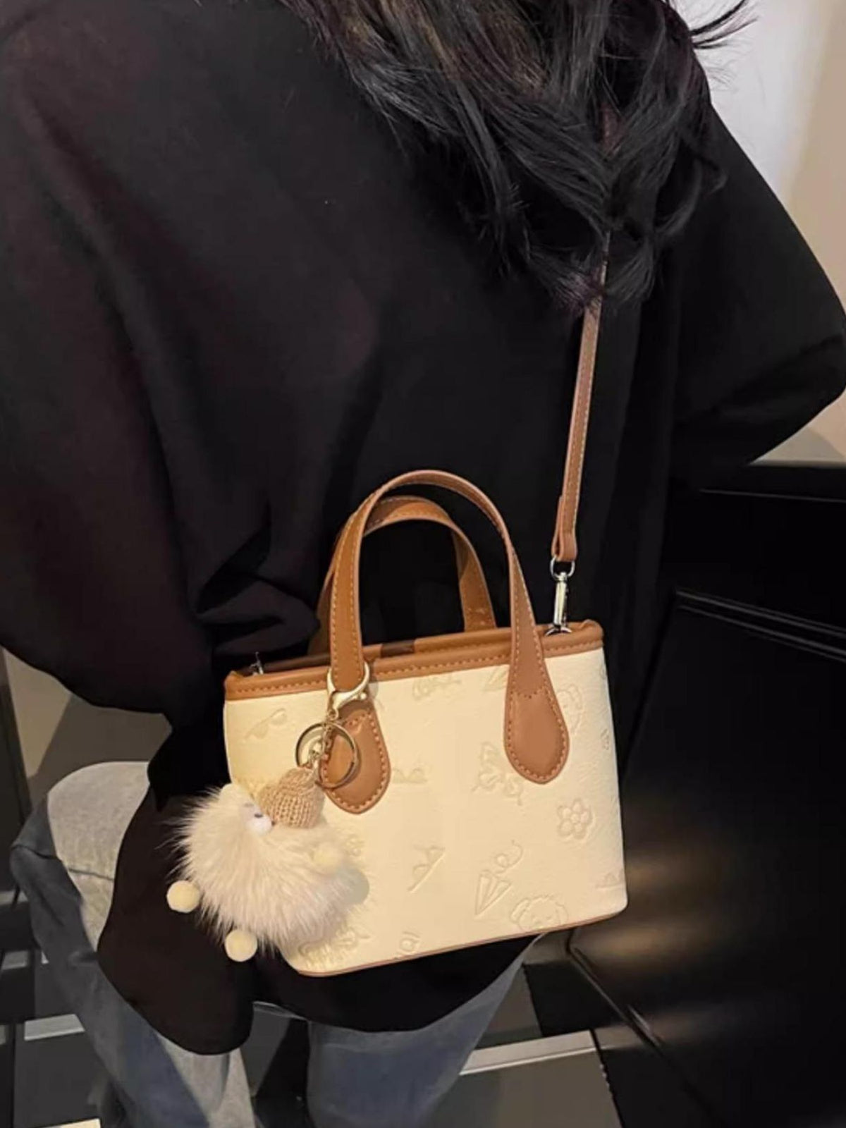 Mini crossbody bag in cream embossed PU leather with tan trim and fuzzy charm.