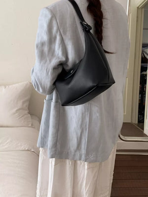 Black crescent hobo bag with a single strap and flap closure, styled with a light blue blazer.