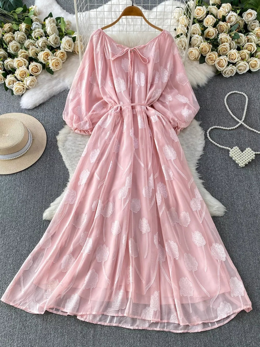 Pink chiffon maxi dress with floral embroidery, puff sleeves, and a tie neck.