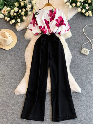 Black wide-leg maternity romper with abstract floral print V-neck top and pockets.