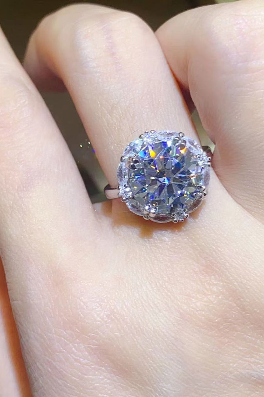 Silver moissanite halo ring with a large round center stone and smaller accent stones.