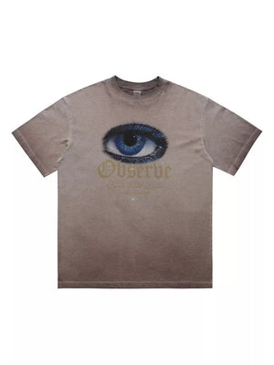 T-shirt in taupe with a graphic of a blue eye and gold text that says Observe.
