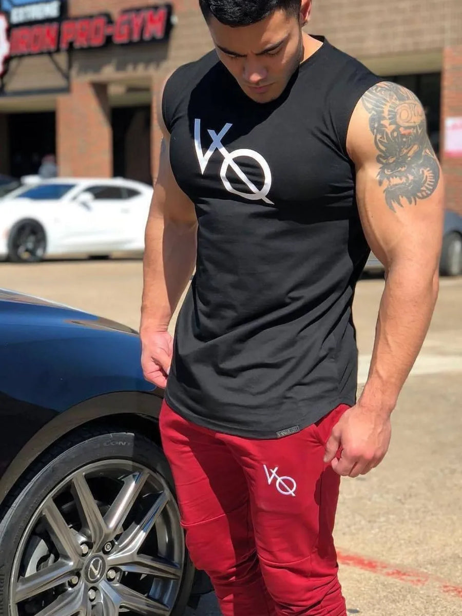 Black graphic muscle tank top with white logo, paired with red joggers.