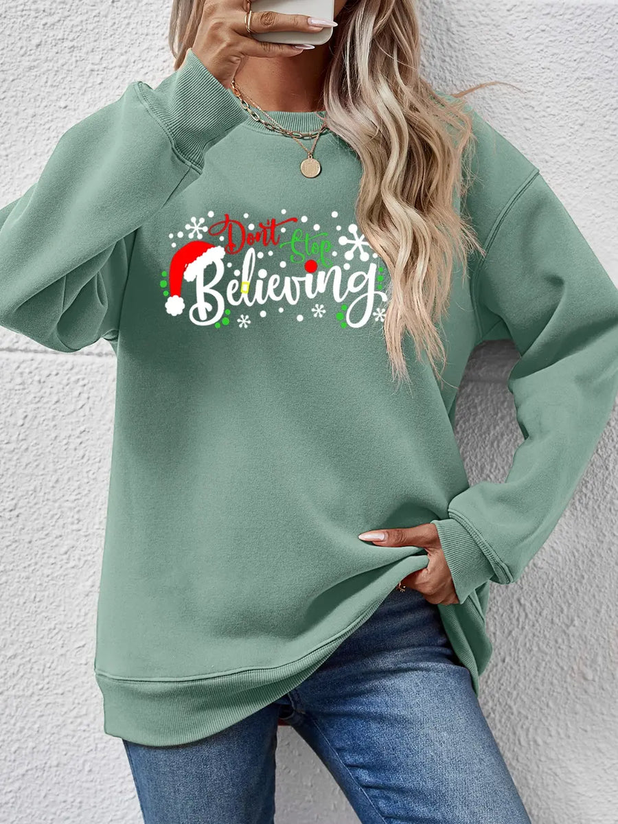Sage green crewneck sweater with "Don't Stop Believing" graphic and Santa hat detail.