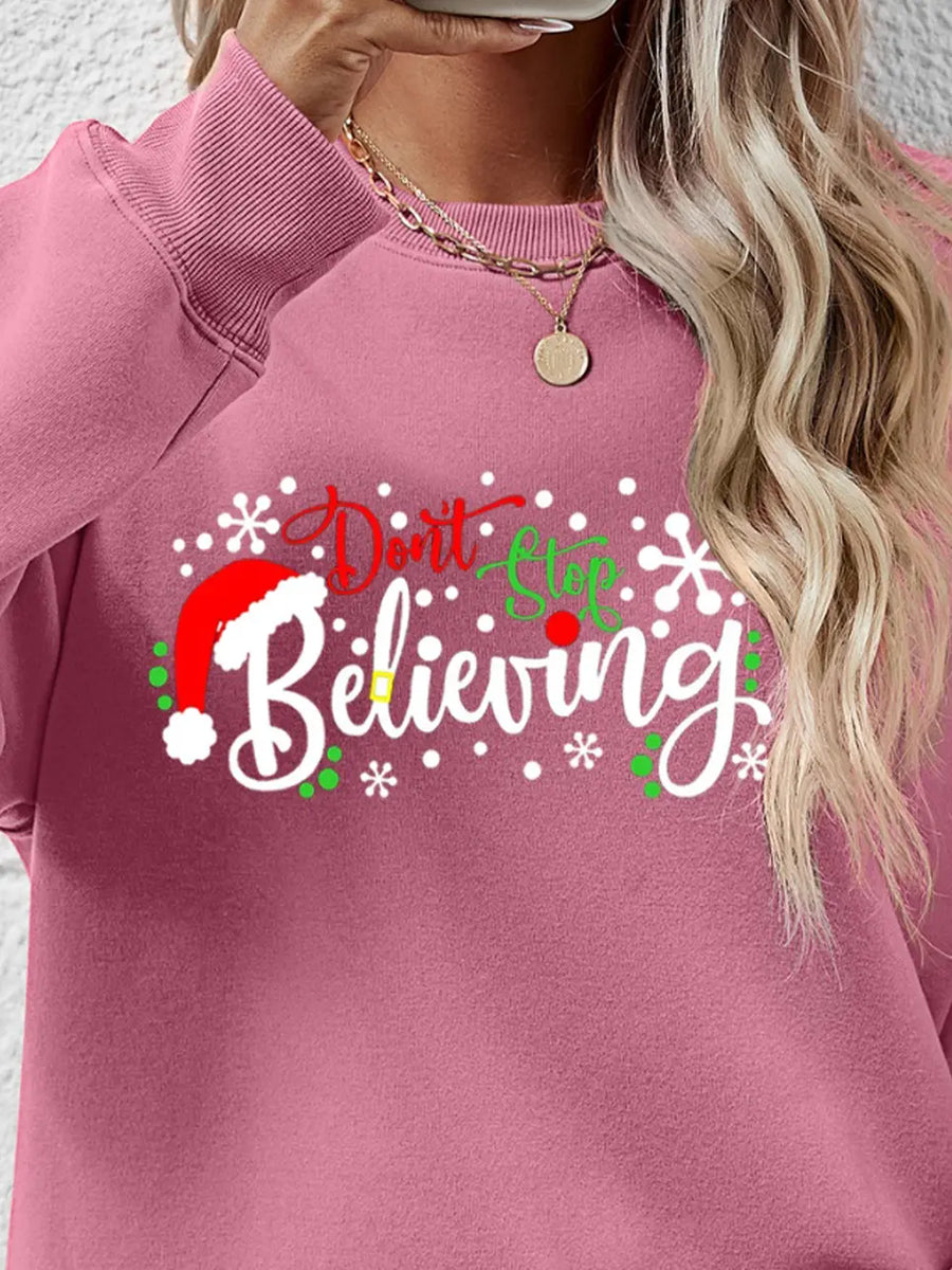 Blush pink long sleeve sweater with "Don't Stop Believing" graphic and Santa hat detail.