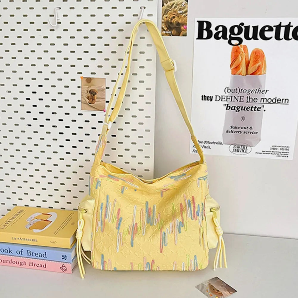 Yellow slouchy shoulder bag with colorful embroidered abstract pattern and side pockets.