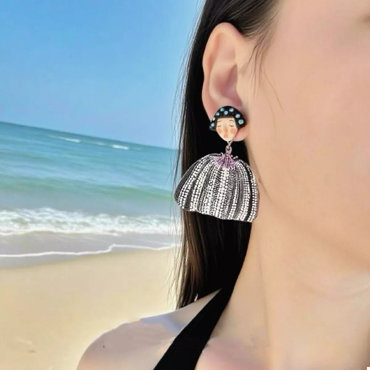 Whimsical girl dangle earrings with black and white patterned skirt and blue gem accents.