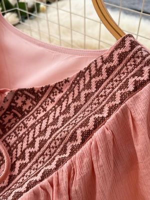 Pink V-neck maxi dress with brown embroidered yoke detail and crinkled fabric.