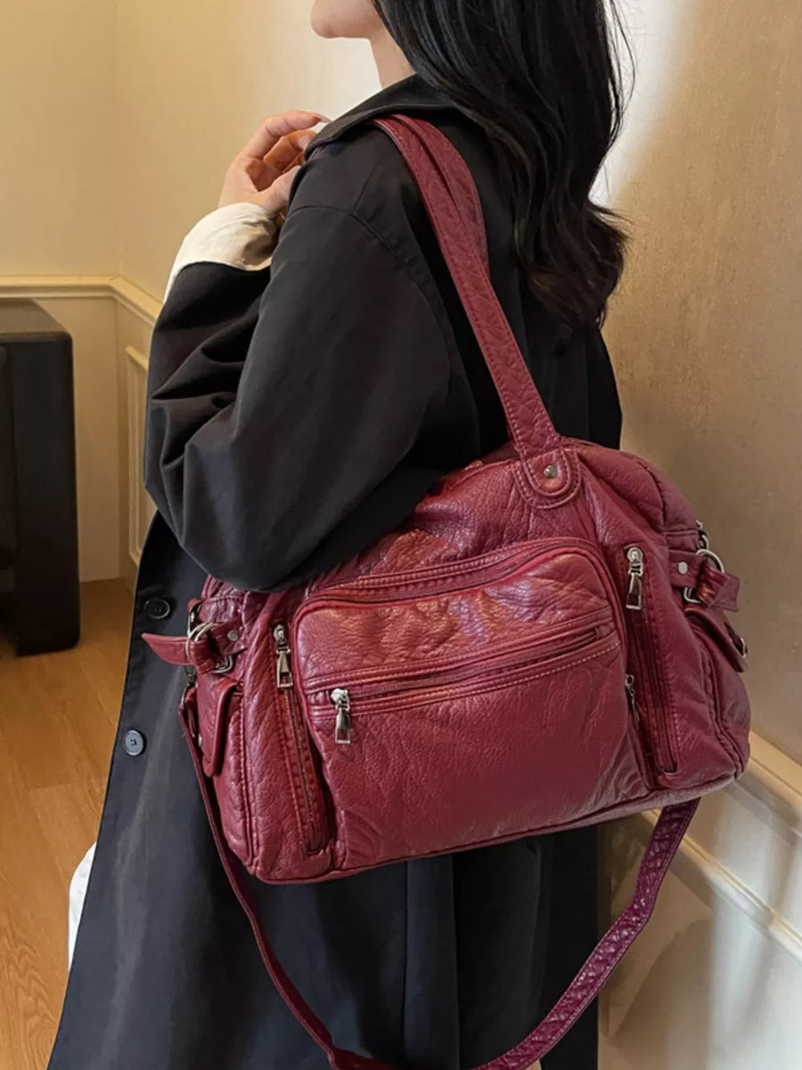 Burgundy faux leather shoulder bag with multiple zippered pockets and adjustable strap.