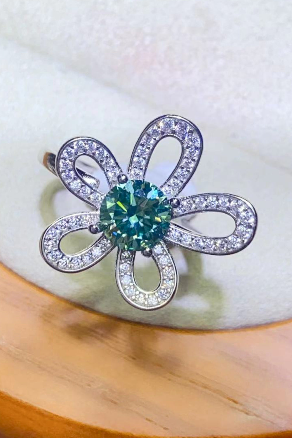 Teal moissanite ring with diamond accents in a flower halo design.
