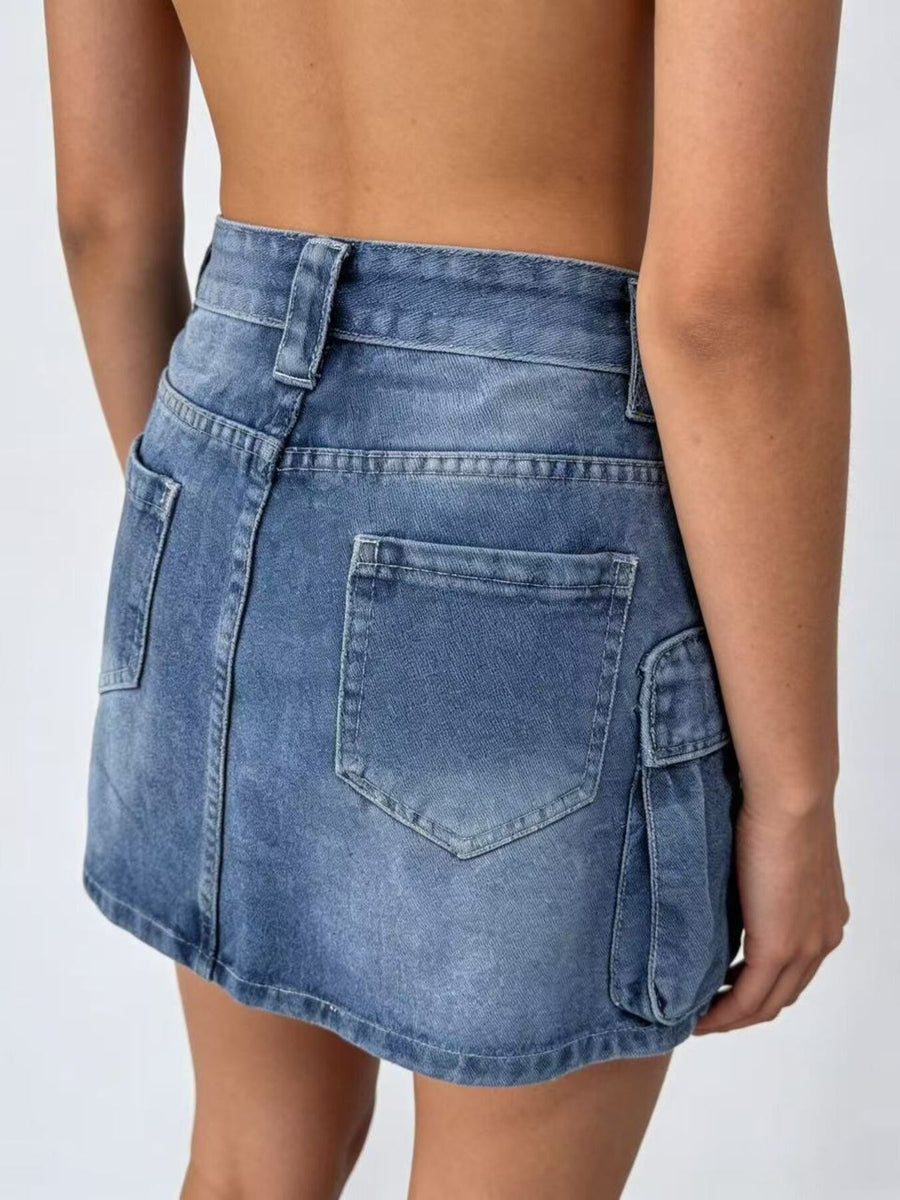 Plus size washed denim cargo skirt in dark blue with button closure and multiple pockets.