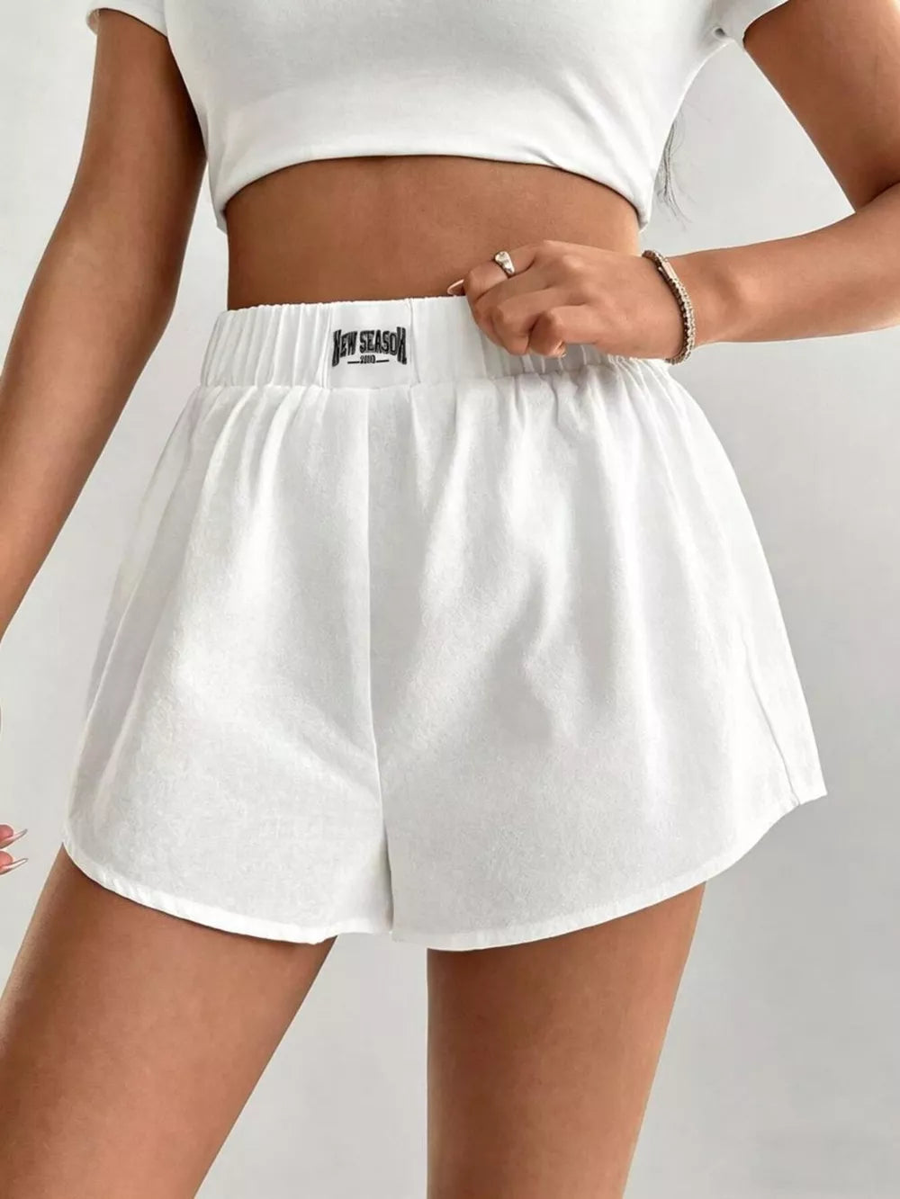 White cotton chino shorts with elastic waistband and curved hem, styled with a crop top.