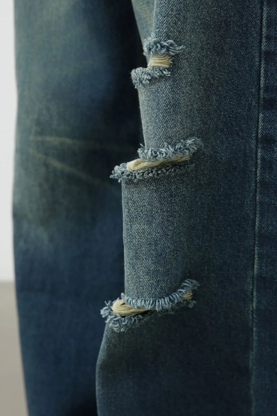 Distressed baggy denim trousers in dark blue with frayed rips and visible stitching.