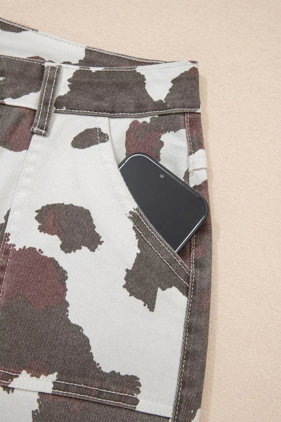 Cow print utility jeans with a phone in the pocket.