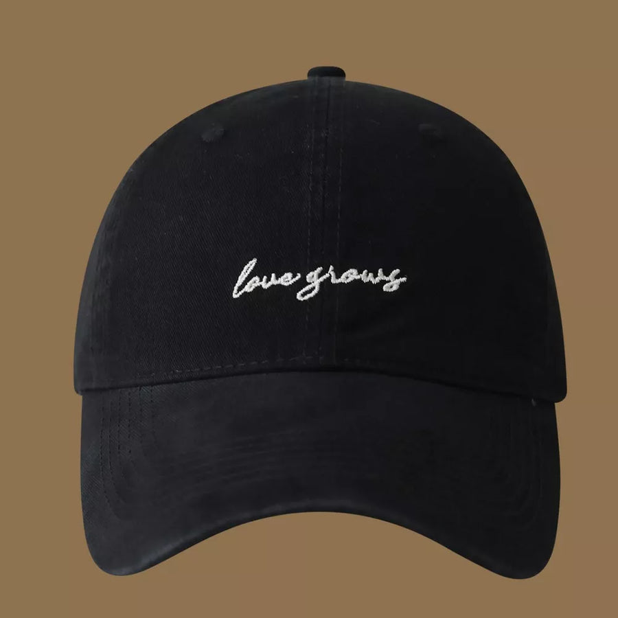 Black cotton baseball cap with embroidered "love grows" text detail.