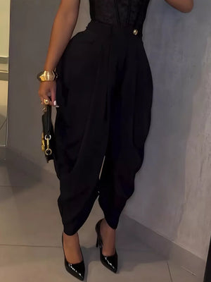 Black sculptural pleated high-waisted pants with a button detail, styled with heels.