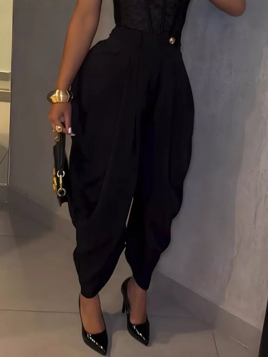 Black sculptural pleated high-waisted pants with a button detail, styled with heels.