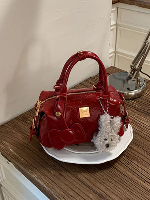 Burgundy crossbody bag with embossed pattern, bow detail, and fluffy dog charm.