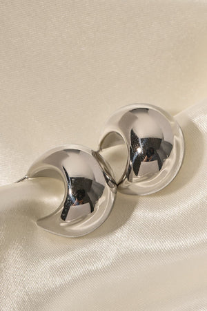 Sculptural silver crescent earrings with a polished finish on a satin background.