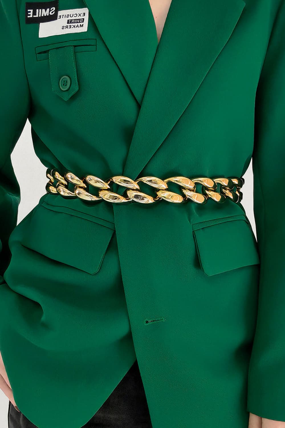 Gold sculptural chain waist belt with large links, worn over a green blazer.