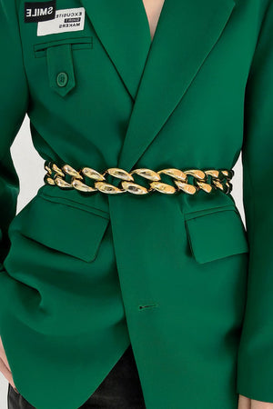 Gold sculptural chain waist belt with large links, worn over a green blazer.