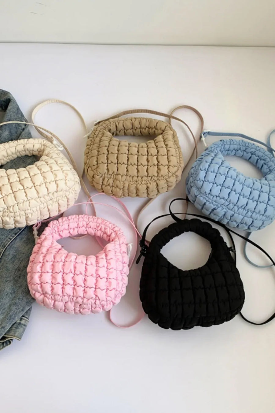 Padded crescent crossbody bags in black, pink, khaki, ivory, and pastel blue with sculptural texture.