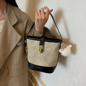 Vintage bucket crossbody bag in tan canvas with black trim and a fuzzy charm.