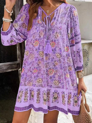 Purple floral mini dress with tassel tie neckline and tiered hem.
