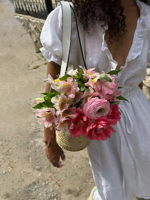 White linen dress with ruffled neckline and puff sleeves, styled with a straw basket bag full of pink flowers.