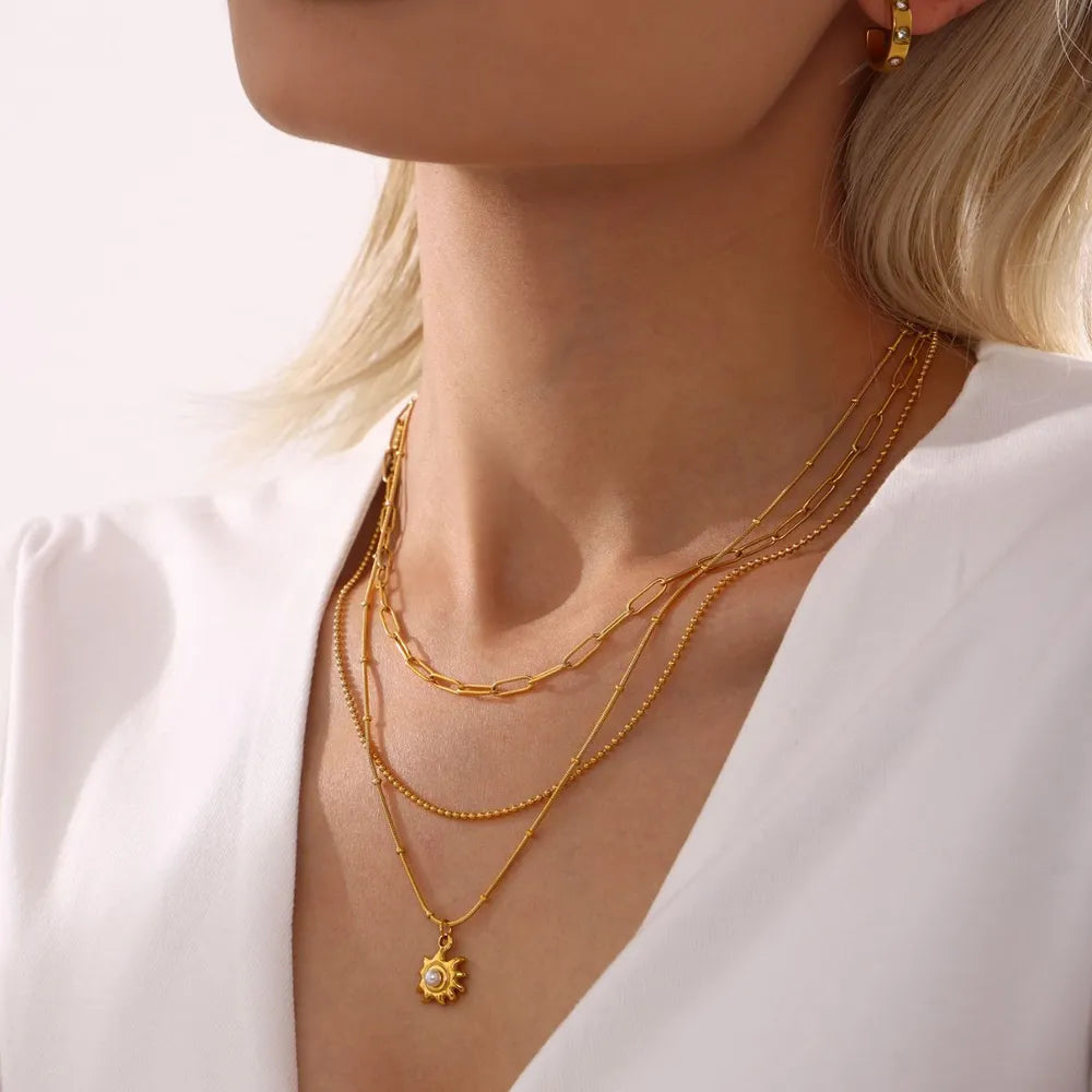Gold layered necklaces with a sunburst pearl pendant and delicate chains.