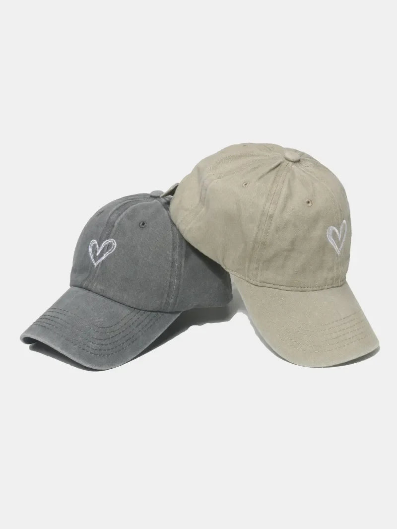 Washed cotton baseball caps in gray and beige, each with a white embroidered heart detail.