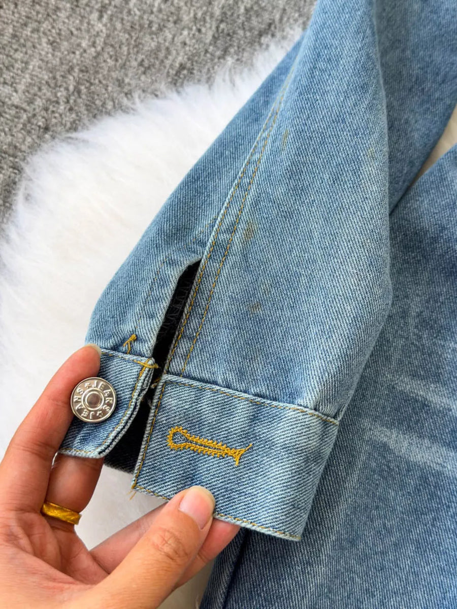 Chic buttoned denim jumpsuit detail with silver button and yellow stitching.