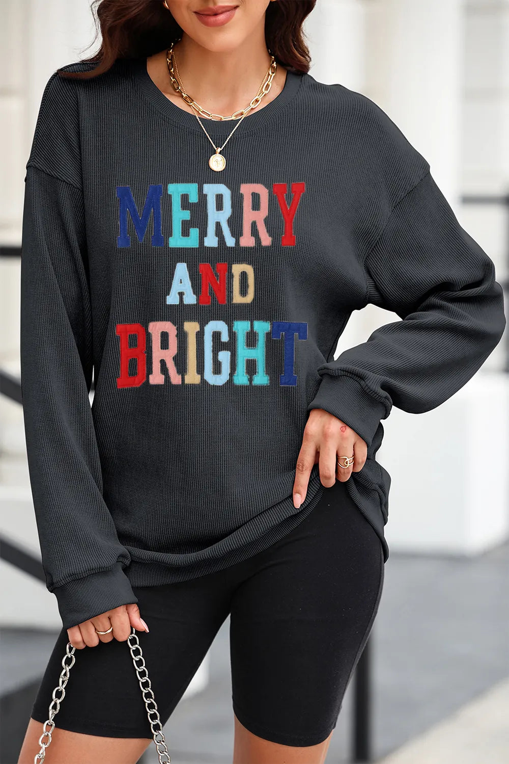 Textured ribbed sweatshirt in black with colorful "Merry and Bright" graphic.