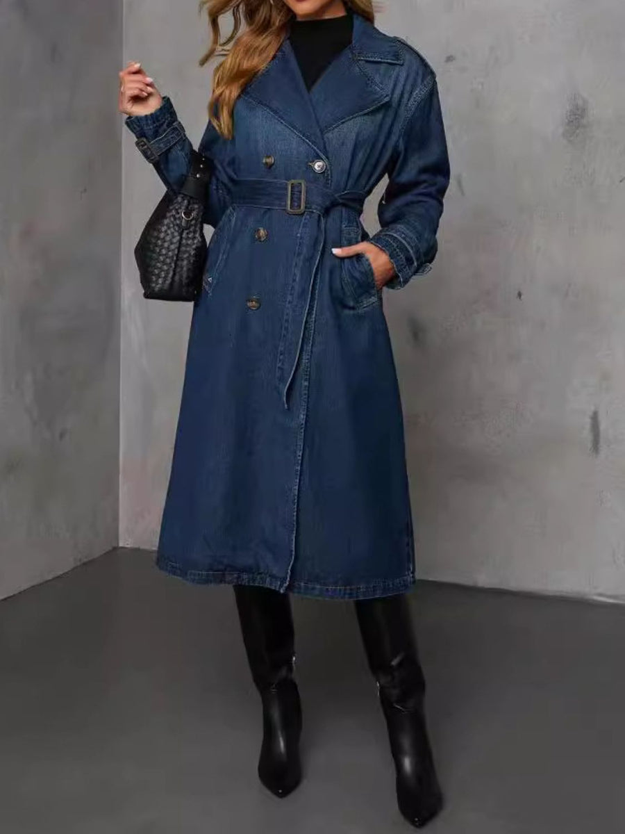 Denim trench coat in dark blue with belted waist, double-breasted buttons, and lapel collar.