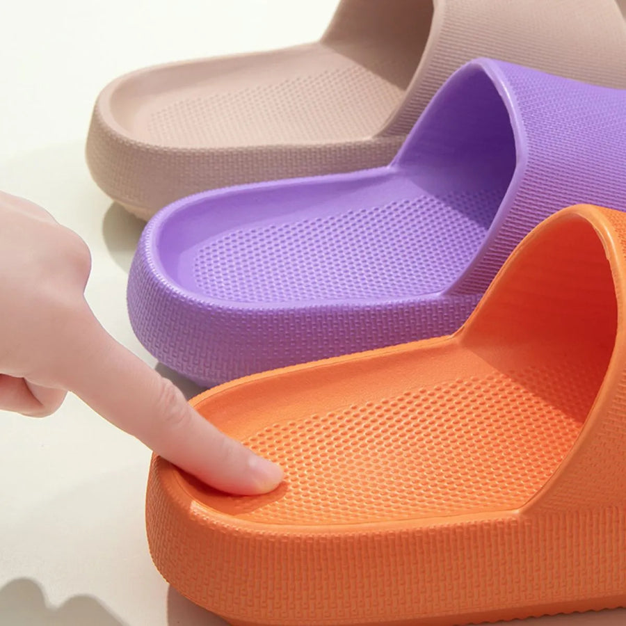 Textured cloud slides slippers in orange, purple, and beige with a finger pressing the orange sole.