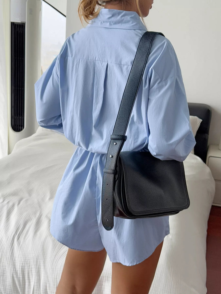 Blue cotton romper with button front and a black crossbody bag.