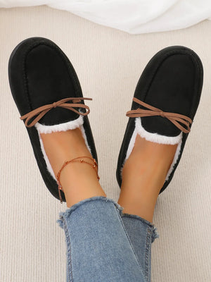 Black suede moccasin slippers with white faux fur lining and brown bow detail.